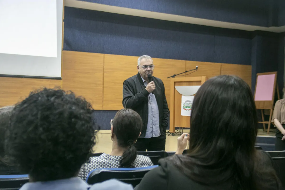 Homem fala ao microfone para servidores sentados na plateia do auditório