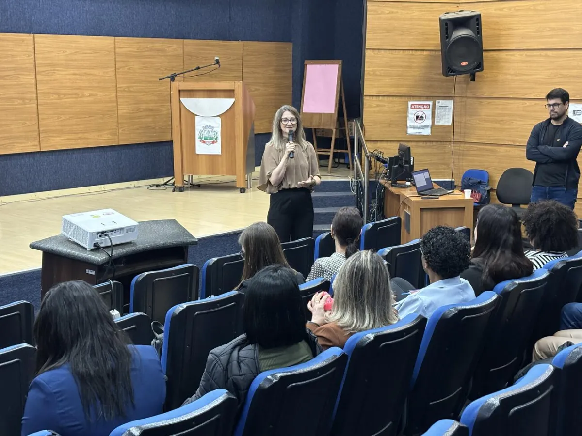 Mulher fala ao microfone para servidores na plateia do auditório
